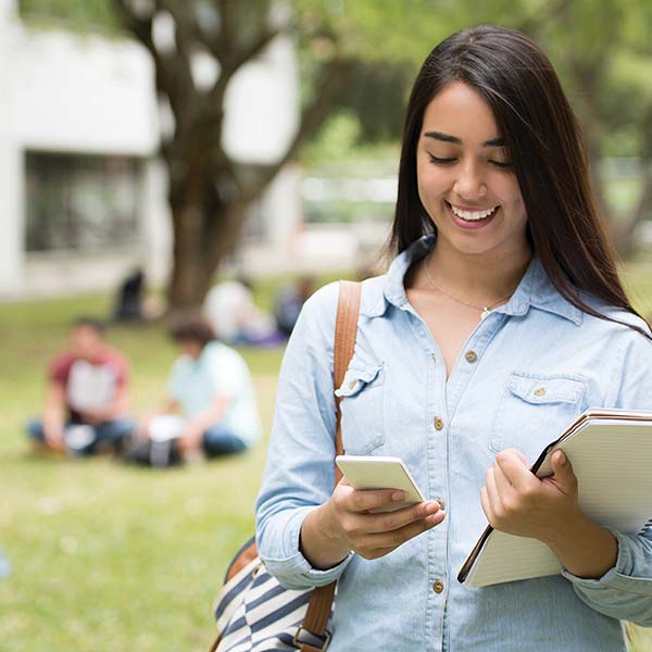a photo of a smiling campus student holding her phone and books