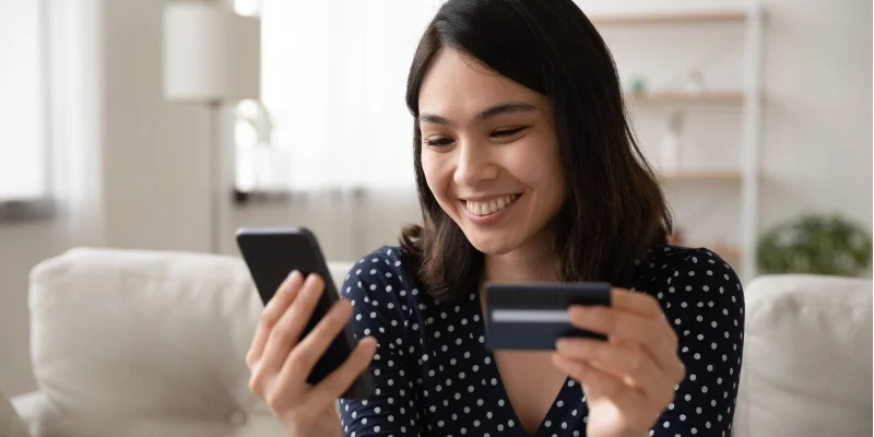a smiling woman holding her phone and credit card