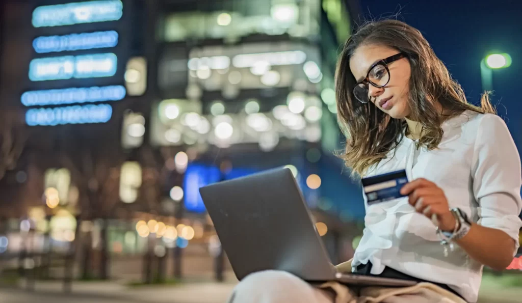 a smiling woman working on her laptop holding a credit card on her left hand