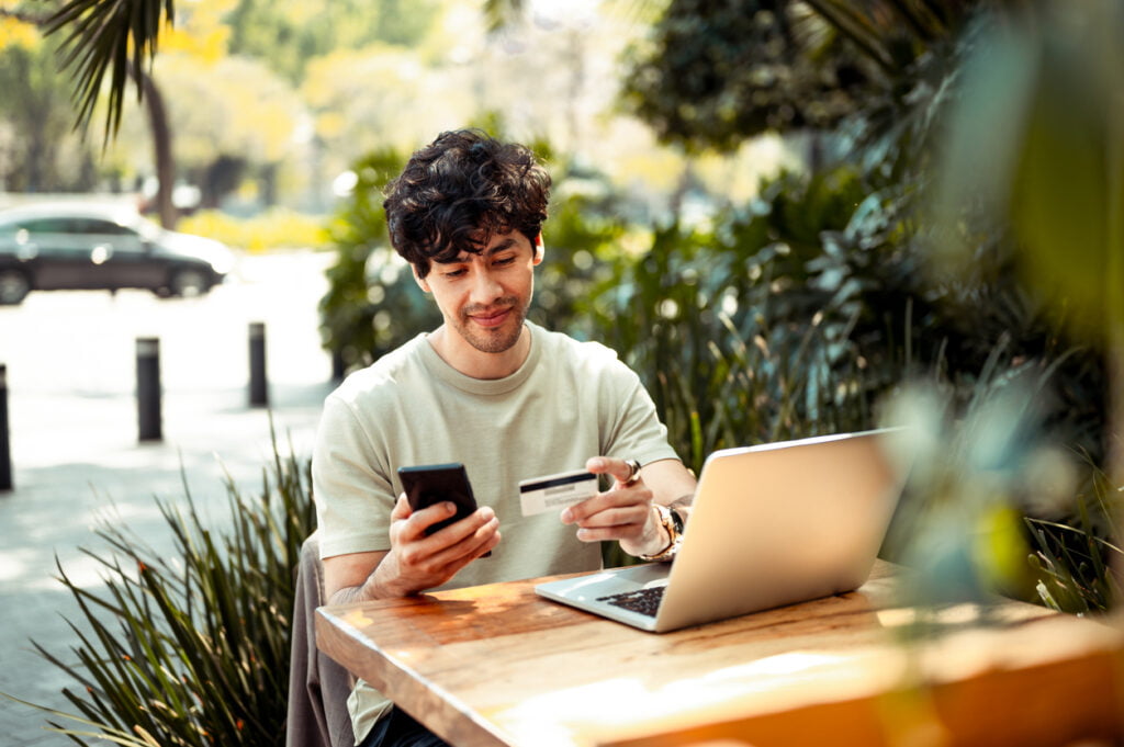 Man holding phone and credit card while online shopping outdoors.