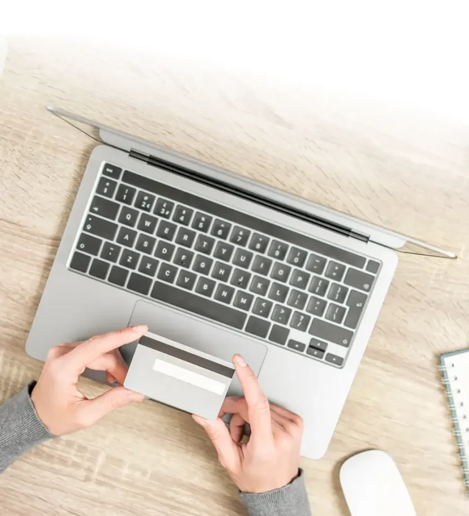 Hands holding a credit card over a laptop for online shopping.